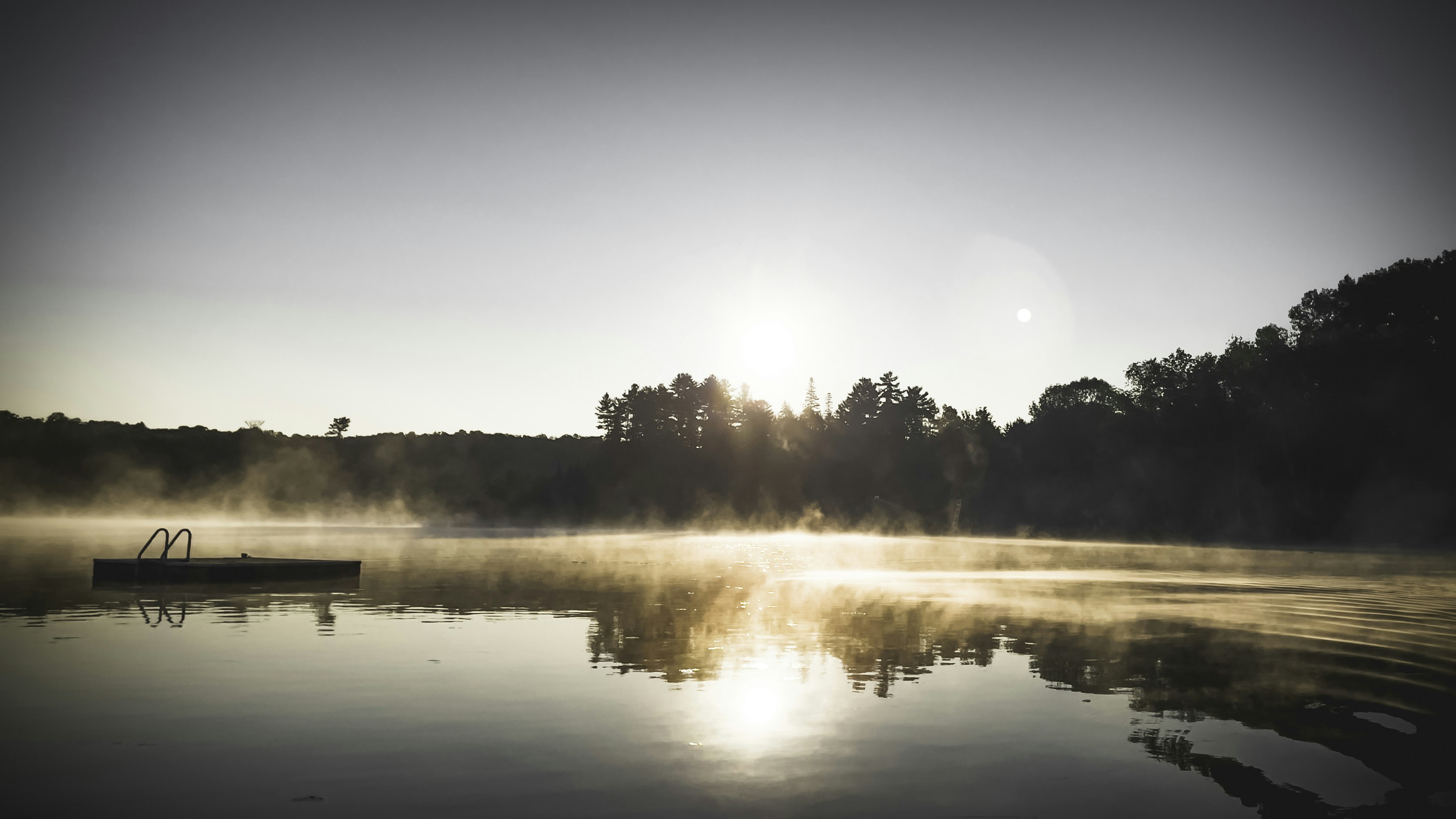 Misty sunrise over a still lake with a small dock